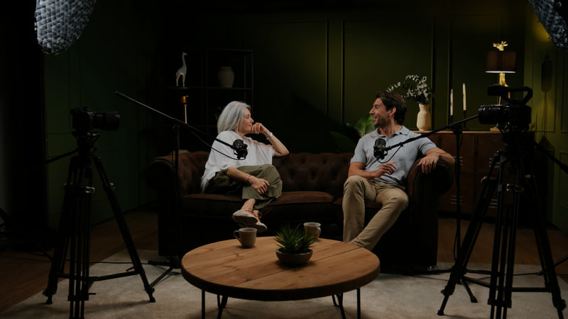 Two cameras on tripods and two boom microphones covering a conversation on a sofa.